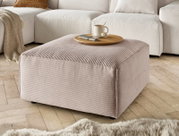Hocker in Nahaufnahme, beige gestreifter Stoff, mit Tablett und Tasse darauf, auf Holzfußboden vor einem Sofa.