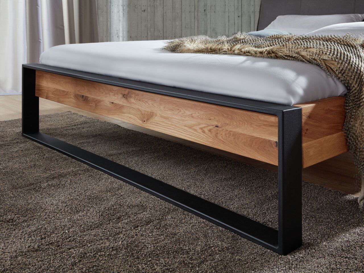 Nahaufnahme eines modernen Balkenbetts mit Holzrahmen und schwarzem Metallgestell, seitliche Perspektive.