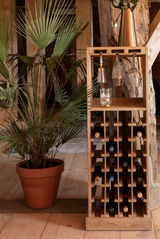 Holz-Weinregal mit mehreren Fächern für Flaschen und Gläser, seitliche Perspektive, neben einer Topfpflanze.