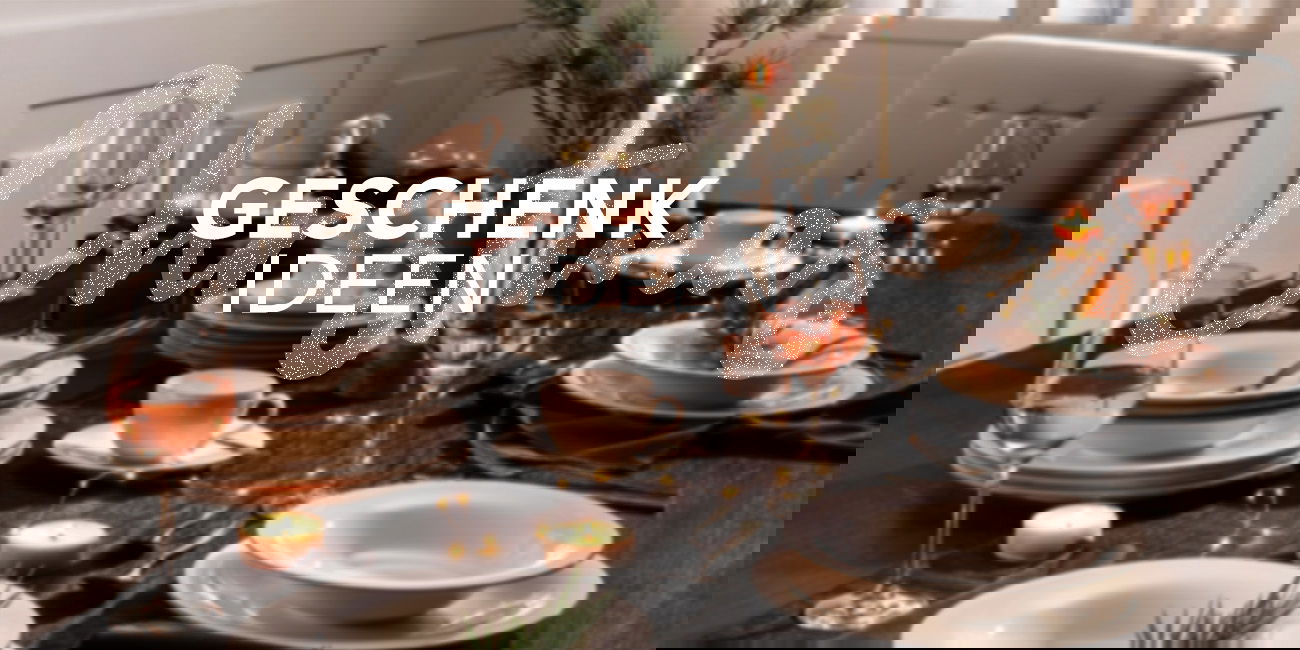 Festlich gedeckter Tisch mit Kerzen und Geschirr, darüber der Schriftzug „Geschenkideen“.