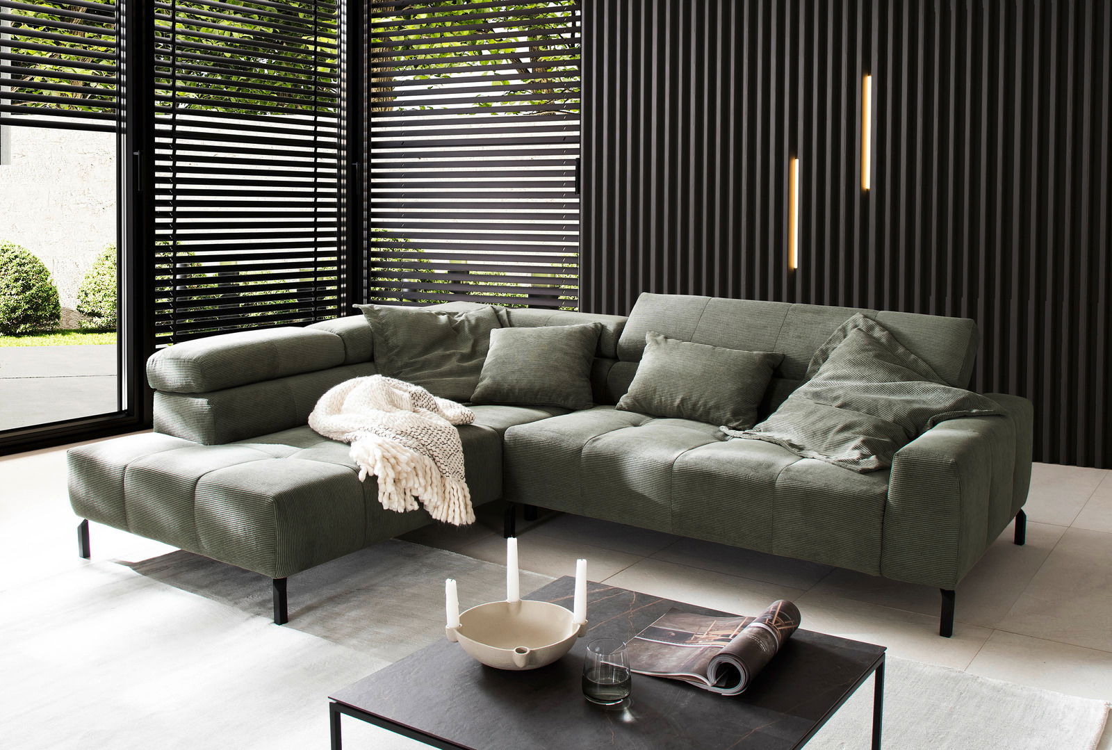 Grüne Ecksofa in modernem Wohnzimmer mit großen Fenstern und stilvoller Dekoration, seitliche Perspektive.