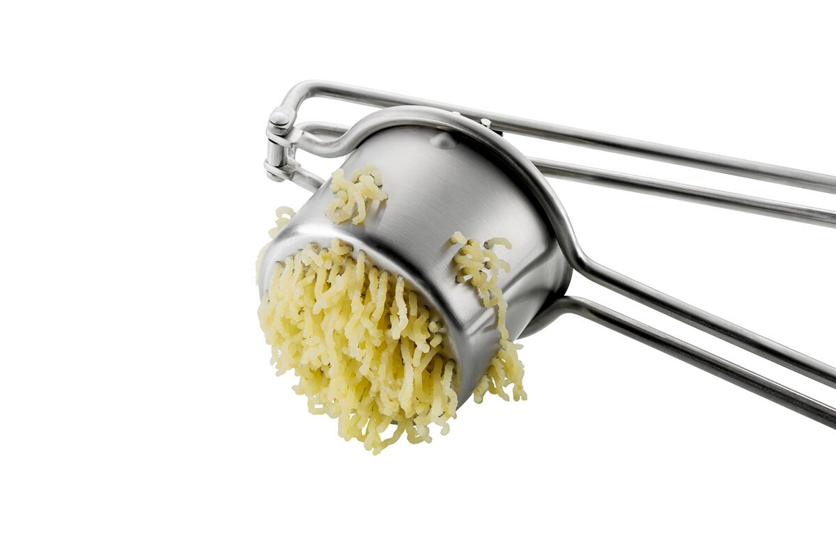 Kartoffel- und Saftpresse Juicy aus Edelstahl, seitliche Perspektive mit gepressten Kartoffeln.
