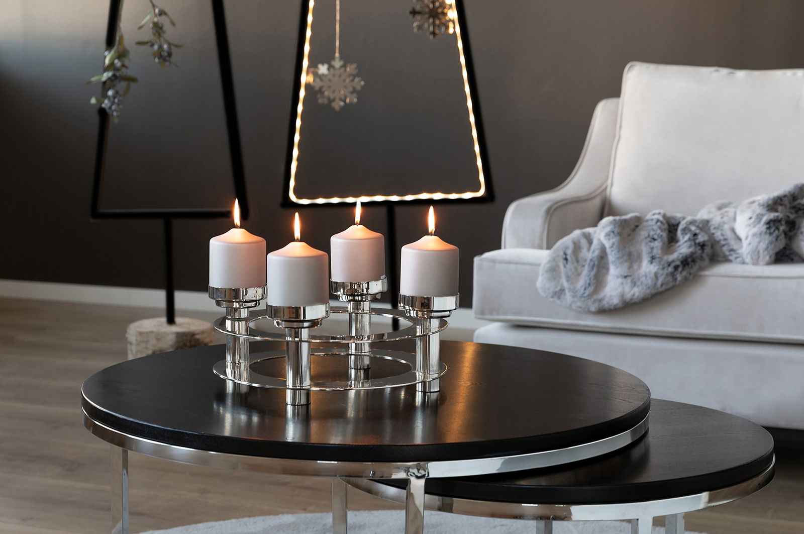 Moderner vierflammiger Kerzenleuchter aus Metall mit weißen Kerzen, auf einem runden Tisch in einem stilvoll eingerichteten Wohnzimmer, seitliche Perspektive.