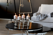Moderner vierflammiger Kerzenleuchter aus Metall mit weißen Kerzen, auf einem runden Tisch in einem stilvoll eingerichteten Wohnzimmer, seitliche Perspektive.