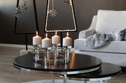 Moderner vierflammiger Kerzenleuchter aus Metall mit weißen Kerzen, auf einem runden Tisch in einem stilvoll eingerichteten Wohnzimmer, seitliche Perspektive.