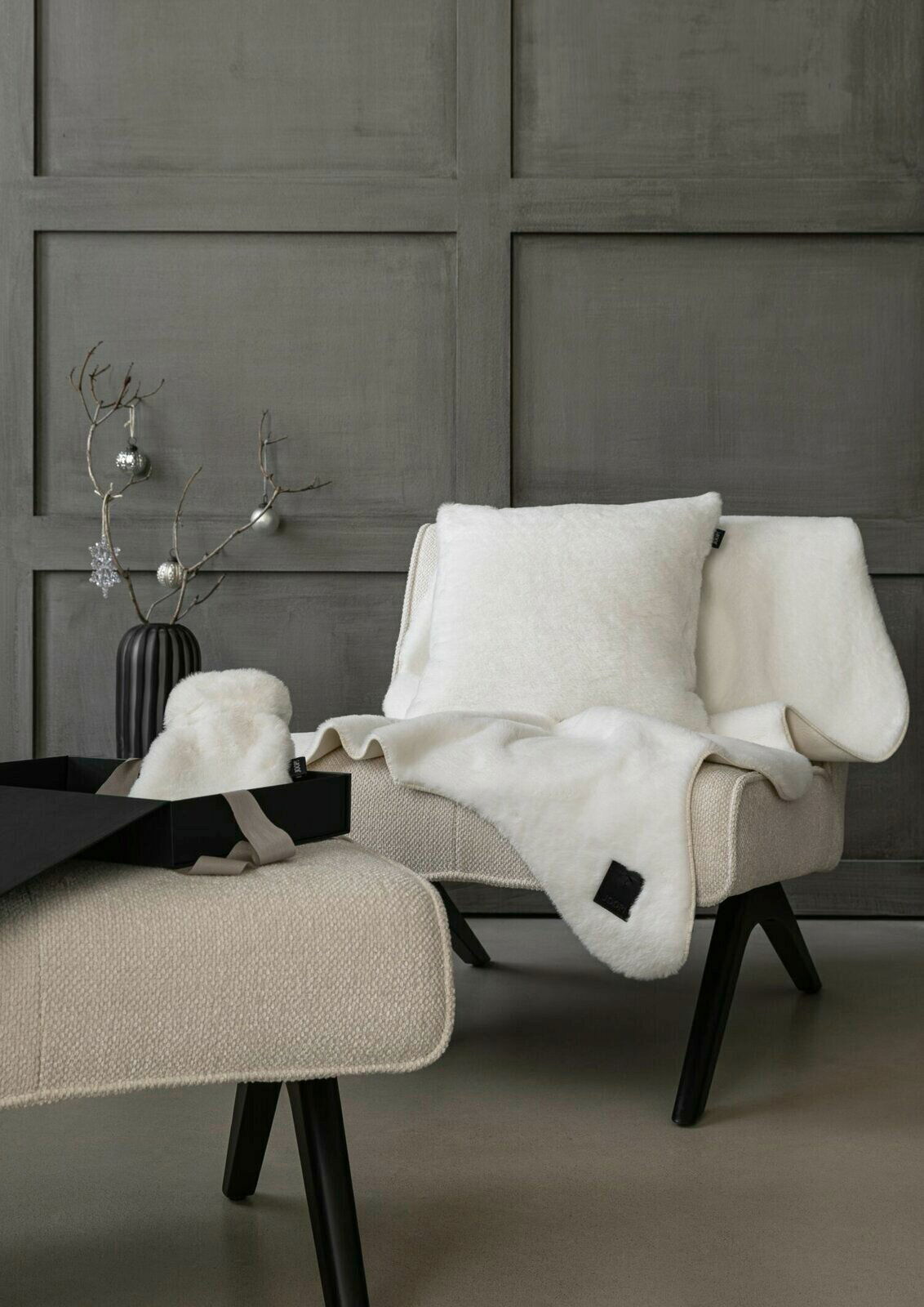 Luxuriöse weiße Wohndecke und Kissen auf einem modernen Sessel in einem stilvollen Raum, seitliche Perspektive.