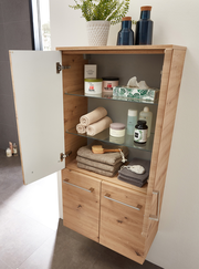 Geöffneter Midischrank aus Holz mit Glaseinlegeböden, gefüllt mit Handtüchern, Pflegeprodukten und Dekoration, aus seitlicher Perspektive fotografiert.