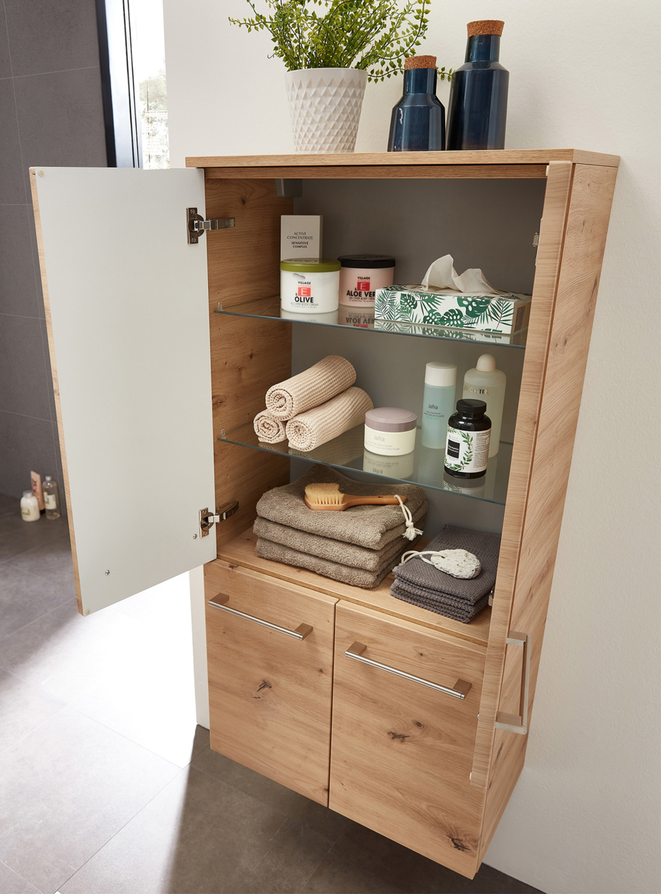 Geöffneter Midischrank aus Holz mit Glaseinlegeböden, gefüllt mit Handtüchern, Pflegeprodukten und Dekoration, aus seitlicher Perspektive fotografiert.