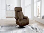Bruine tv-fauteuil met een modern ontwerp, geplaatst op een zilveren draaischijf, in een lichte woonkamer met kunst en beeldhouwwerken op de achtergrond, gezien vanuit een zijdelingse hoek.