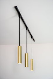 Drei zylindrische Pendelleuchten in mattgoldener Farbe, von einer schwarzen Schiene an der Decke hängend, aus seitlicher Perspektive fotografiert.