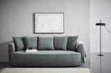 Graues Funktionssofa mit Kissen, frontal fotografiert, vor einer grauen Wand mit abstraktem Kunstwerk und einer Stehlampe.