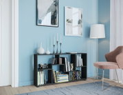 Schwarzes, niedriges Regal mit asymmetrischen Fächern und Büchern, dekoriert mit weißen Vasen und Kerzenhaltern, im modernen Wohnzimmer vor hellblauer Wand – Perspektive: frontale Ansicht mit leichtem Blick von rechts.