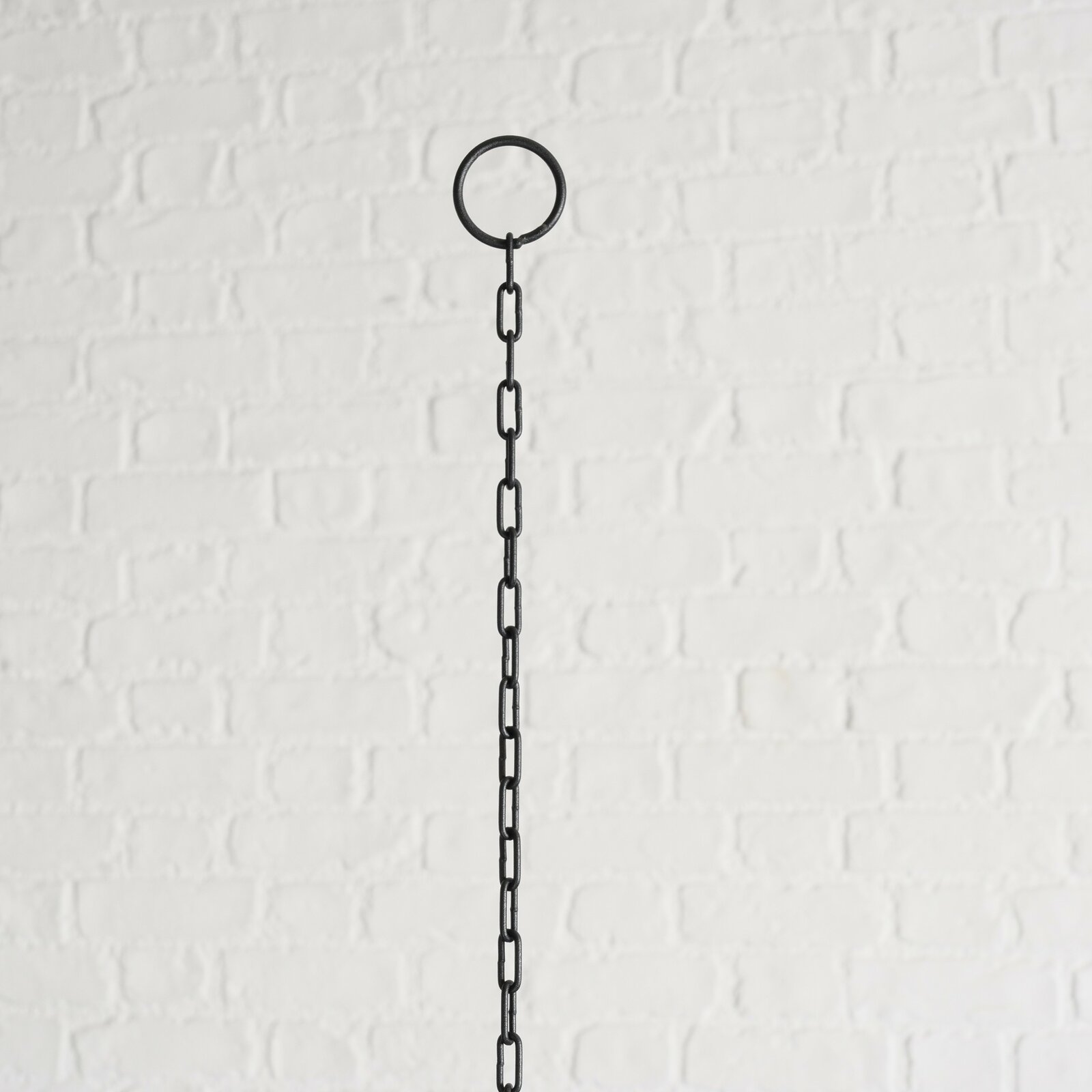 Schwarze Metallkette mit Ring, vor weißer Ziegelwand, von unten nach oben fotografiert