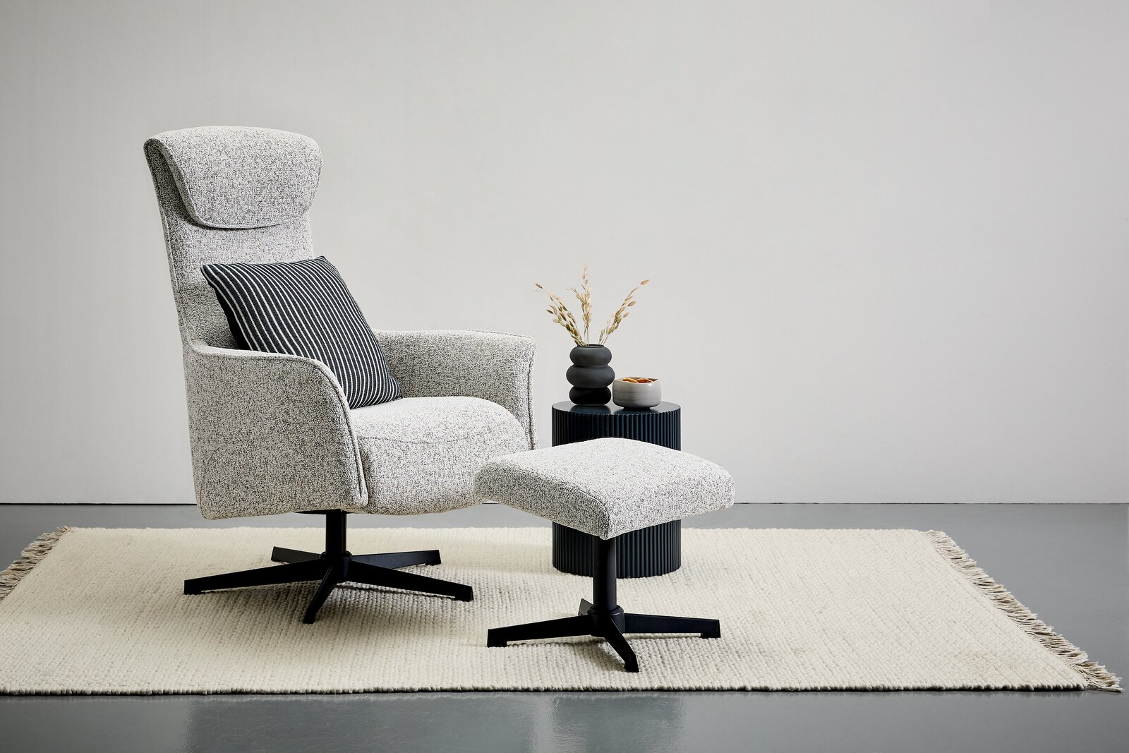 Seitenansicht eines modernen Relaxsessels mit Hocker auf einem Teppich, begleitet von einem kleinen Beistelltisch mit Dekoration.