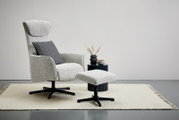 Seitenansicht eines modernen Relaxsessels mit Hocker auf einem Teppich, begleitet von einem kleinen Beistelltisch mit Dekoration.