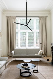 Moderner Wohnraum mit drei runden Beistelltischen in verschiedenen Höhen, zentral im Bild platziert. Im Hintergrund ein großes Fenster mit Vorhängen und ein graues Sofa. Perspektive von vorne.