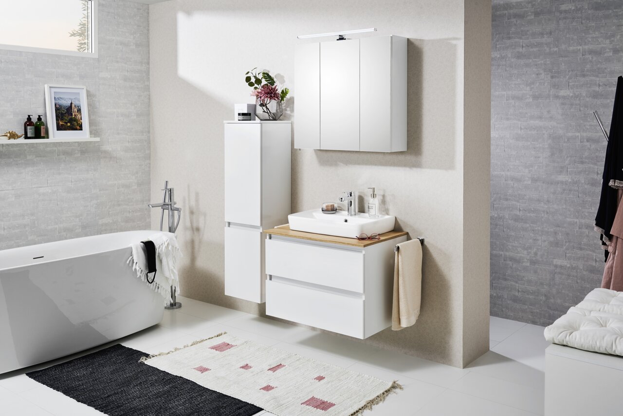 Moderne badkamer met een witte, aan de muur bevestigde wastafel met houten plank en opzetwastafel, bijpassende spiegelkast met ledverlichting en hoge zijkast; perspectief: vooraanzicht met een lichte zijaanzicht.