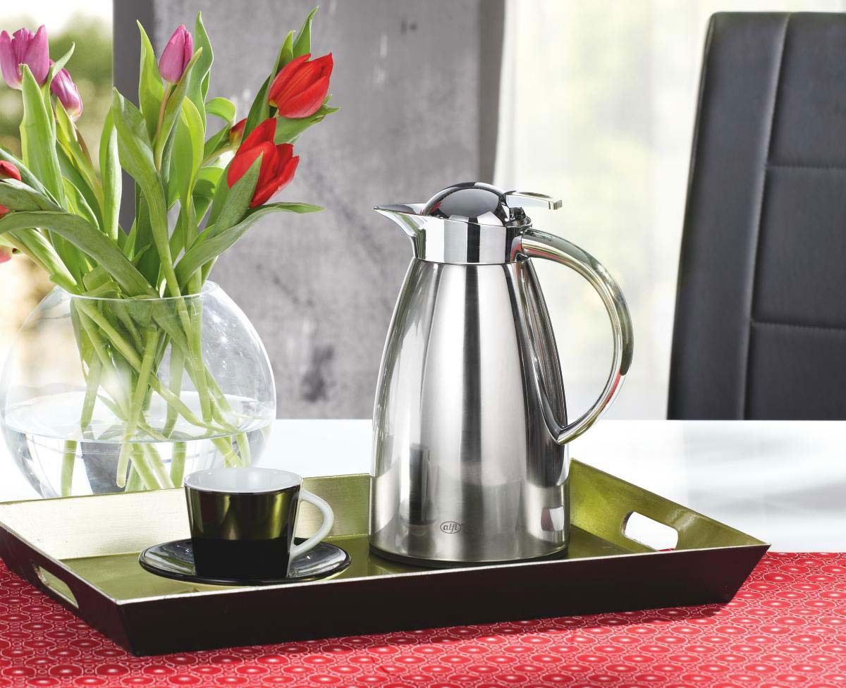 Edelstahl-Isolierkanne Signo auf einem Tablett, umgeben von einer Tasse und einem Blumenstrauß, seitliche Perspektive
