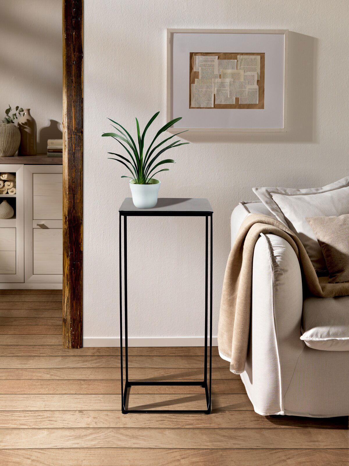 Moderner Beistelltisch mit schwarzem Metallgestell und quadratischer Tischplatte, darauf steht eine grüne Pflanze in einem weißen Topf. Perspektive: Frontalansicht.