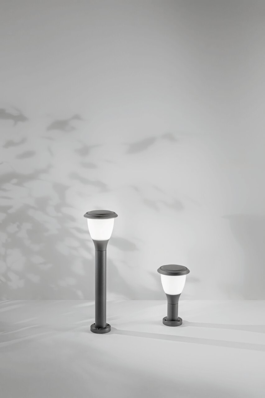 Zwei moderne Pollerleuchten der Serie Fabas Luce THIAGO in unterschiedlichen Höhen, frontal betrachtet, vor einem Hintergrund mit Schatten von Blättern.