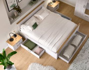 Weißes Doppelbett in Holzoptik mit integrierten, ausgezogenen Schubladen zur Aufbewahrung, aufgenommen aus schräger Vogelperspektive von oben in einem hellen Schlafzimmer.