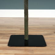 Nahaufnahme des unteren Teils eines beschneiten künstlichen Tannenbaums mit stabilem Metallständer auf Holzfußboden.