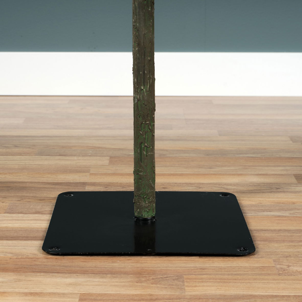 Nahaufnahme des unteren Teils eines beschneiten künstlichen Tannenbaums mit stabilem Metallständer auf Holzfußboden.