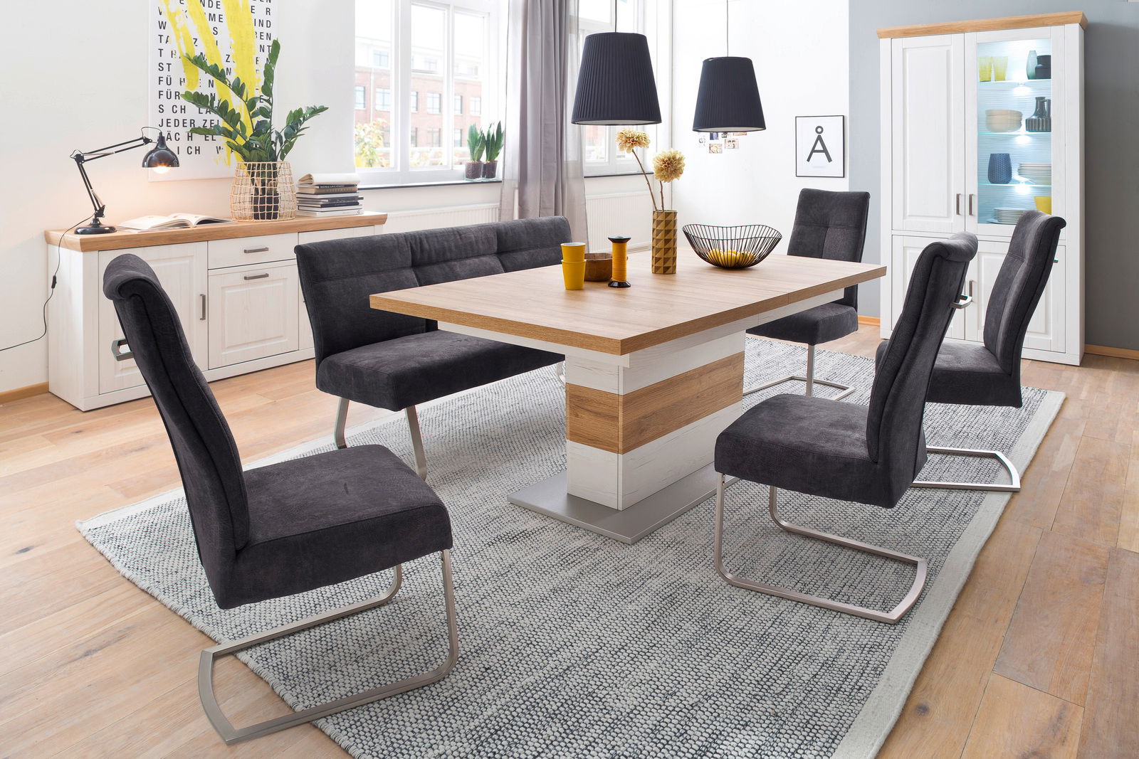 Moderner Esstisch mit Holz- und Weißakzenten, umgeben von sechs grauen Stühlen in einem hellen Esszimmer mit großen Fenstern, aus seitlicher Perspektive.