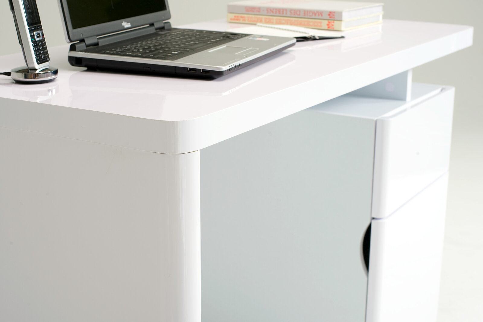 Moderner weißer Schreibtisch mit abgerundeten Ecken, Laptop und Büchern, seitliche Perspektive