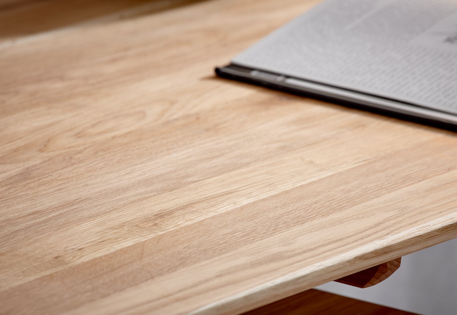 Close-up van een bureau van licht hout met een open tijdschrift op de rand, gefotografeerd vanuit een schuin perspectief.