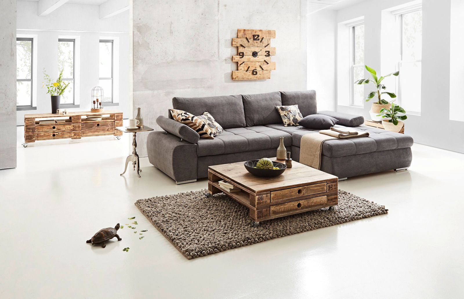 Graues Ecksofa INFERNO in modernem Wohnzimmer, Perspektive von vorne rechts, mit Holztisch und Dekoration.