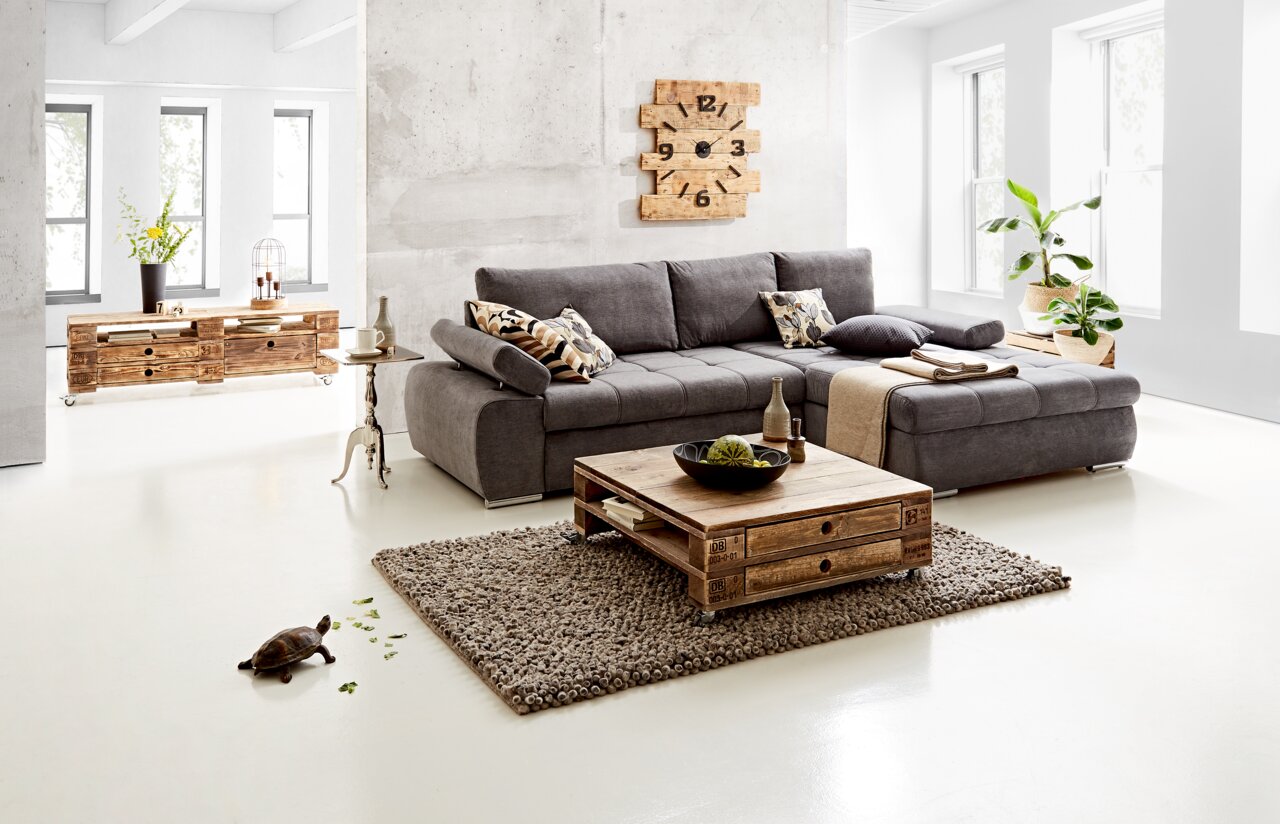 Graues Ecksofa INFERNO in modernem Wohnzimmer, Perspektive von vorne rechts, mit Holztisch und Dekoration.