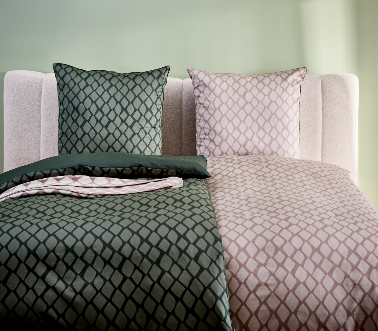 Wendebettwäsche mit geometrischem Muster in Grün und Beige, auf einem Bett mit hellgrüner Wand im Hintergrund, aus der Vorderansicht fotografiert.