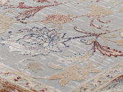 Nahaufnahme eines Orientteppichs mit floralen Mustern in Rot, Blau und Beige auf grauem Hintergrund, aus schräger Perspektive aufgenommen.