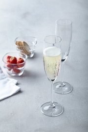 Twee elegante champagneglazen, waarvan één gevuld met bruisende champagne, op een tafel met aardbeien en koekjes op de achtergrond, gefotografeerd vanuit een licht verhoogd perspectief.
