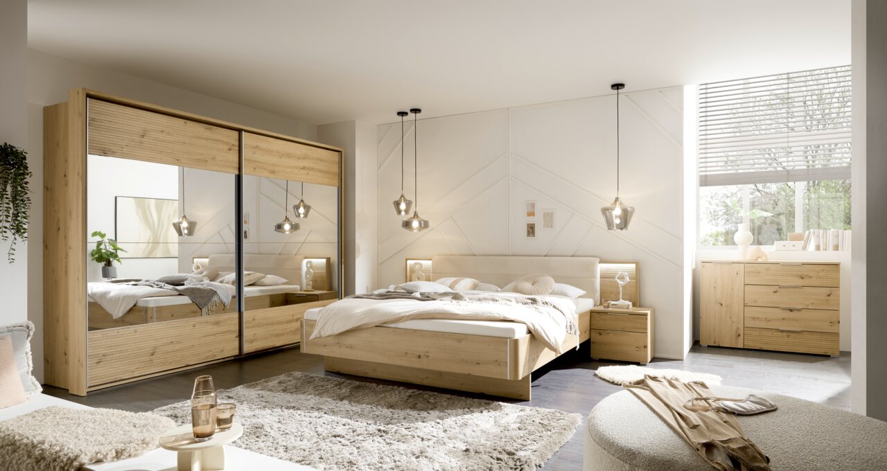 Moderner Schwebetürenschrank mit zwei Türen in Holzoptik, frontal im Schlafzimmer mit Bett und Nachttischen, beleuchtet durch hängende Lampen.