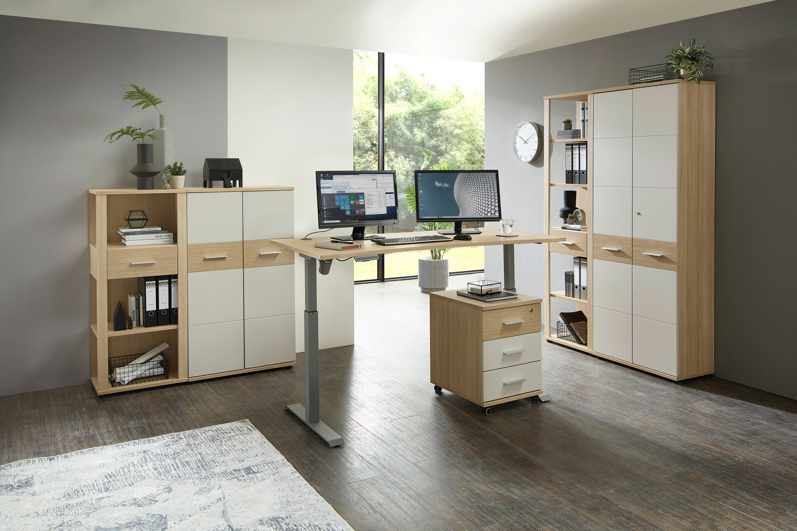 Moderner höhenverstellbarer Schreibtisch mit zwei Monitoren, umgeben von Aktenschränken und Regalen in einem hellen Büro mit Blick auf den Garten. Perspektive: Frontalansicht.
