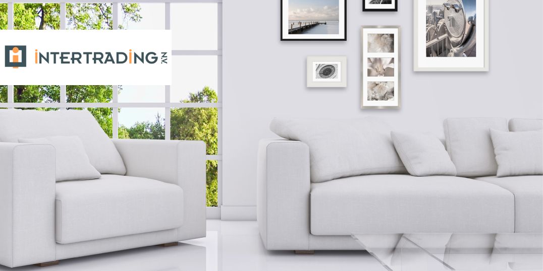 Modernes Wohnzimmer mit weißen Sofas, einem Glastisch und gerahmten Kunstwerken vor einer hellen Fensterfront mit Grünpflanzen.