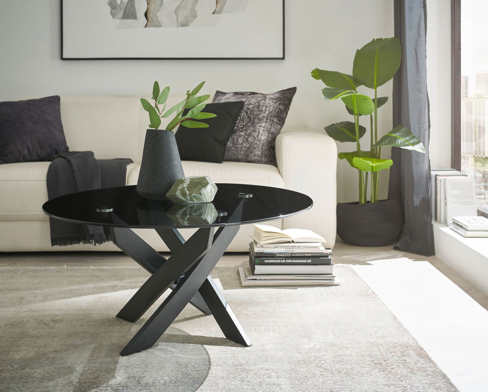 Zurbrüggen Couchtisch 2 KOPENHAGEN Moderner Couchtisch mit schwarzer Glasplatte und gekreuztem Metallgestell, seitliche Perspektive im Wohnzimmer mit Sofa und Pflanzen.