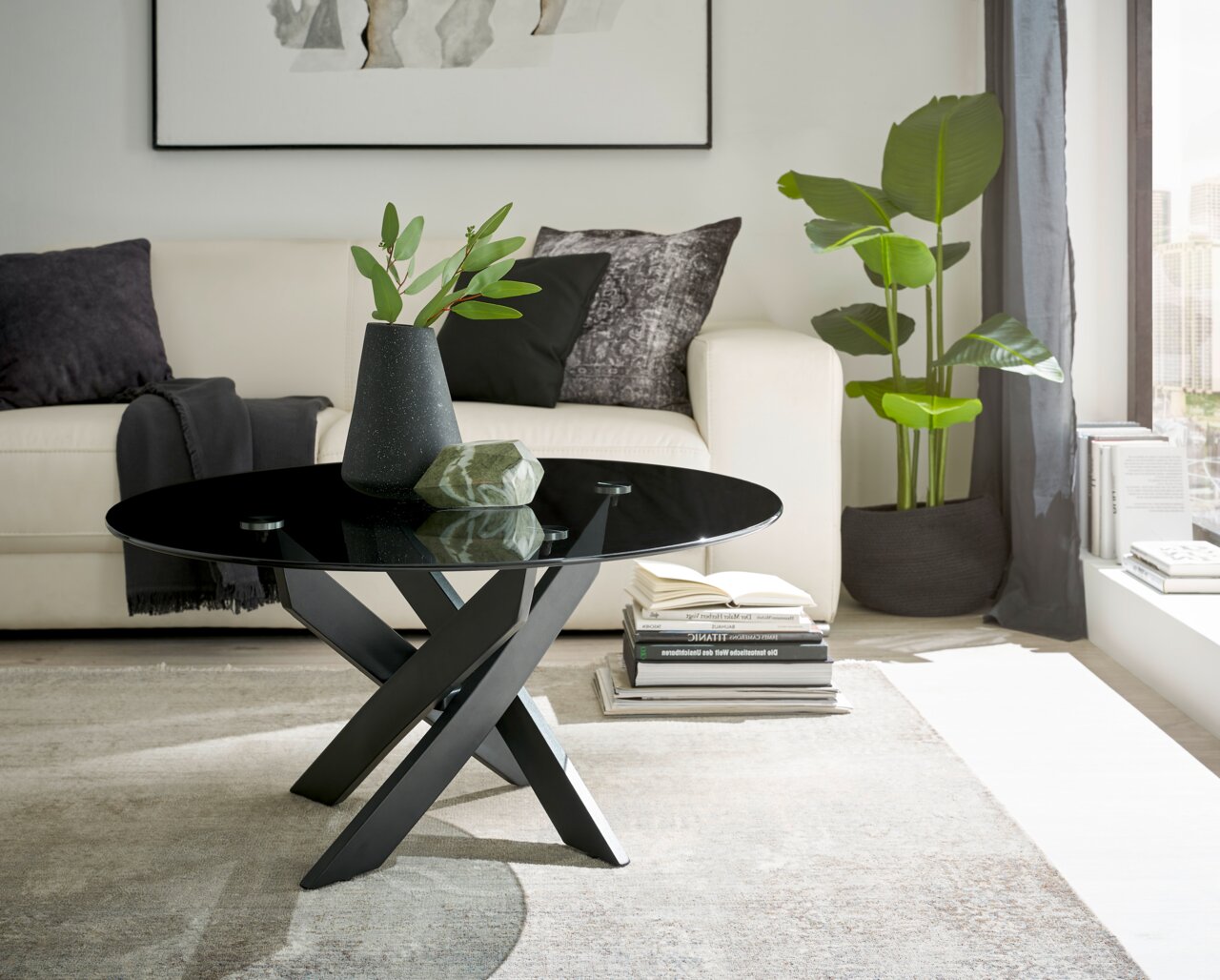 Zurbrüggen Couchtisch 2 KOPENHAGEN Moderner Couchtisch mit schwarzer Glasplatte und gekreuztem Metallgestell, seitliche Perspektive im Wohnzimmer mit Sofa und Pflanzen.