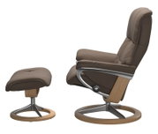 Zijaanzicht van een bruine fauteuil met bijpassende voetenbank, beide met een frame van hout en metaal.