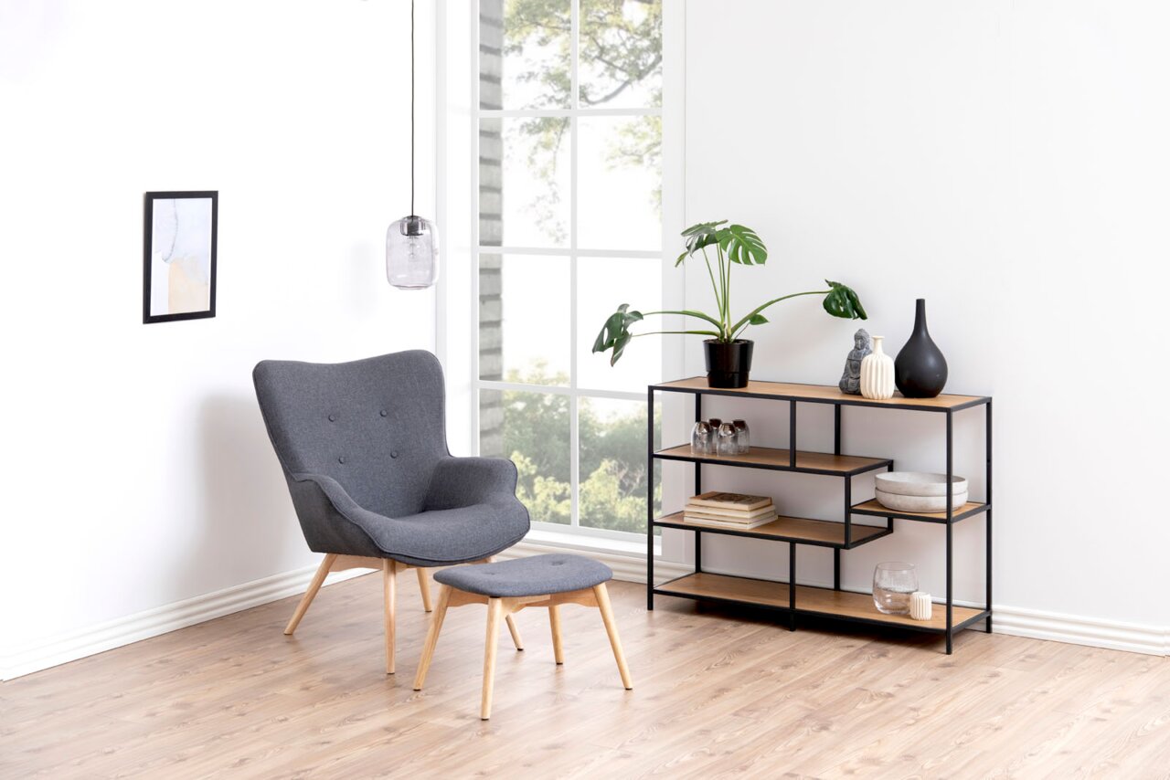 Modernes Bücherregal mit schwarzem Metallrahmen und Holzböden, seitliche Perspektive, dekoriert mit Pflanzen und Vasen, in einem hellen Raum mit Sessel und Hocker.