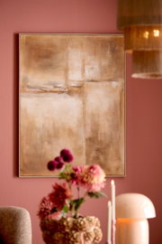 Frontaal aanzicht van een groot abstract schilderij in warme beige- en bruintinten, stijlvol opgehangen aan een oudroze muur boven een tafel met bloemen, kaarsen en een tafellamp.