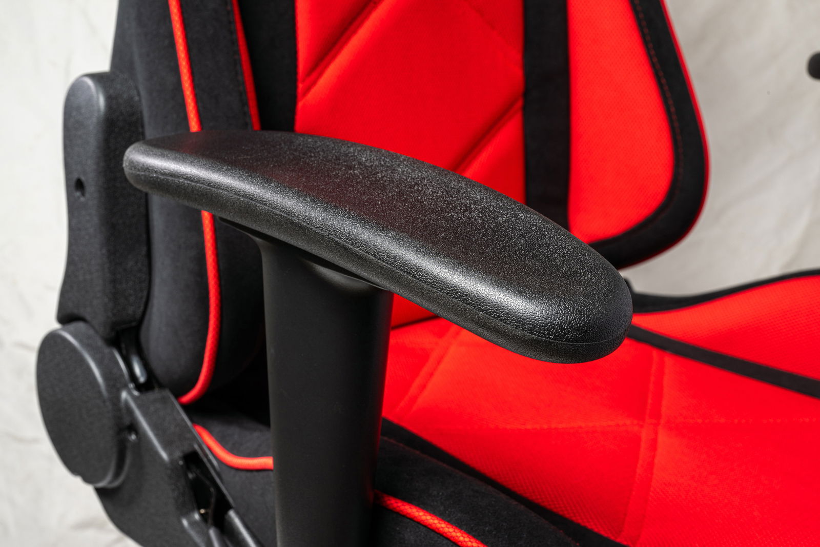 Nahaufnahme eines Gaming-Stuhls mit rotem Stoff und schwarzer Armlehne, seitliche Perspektive.