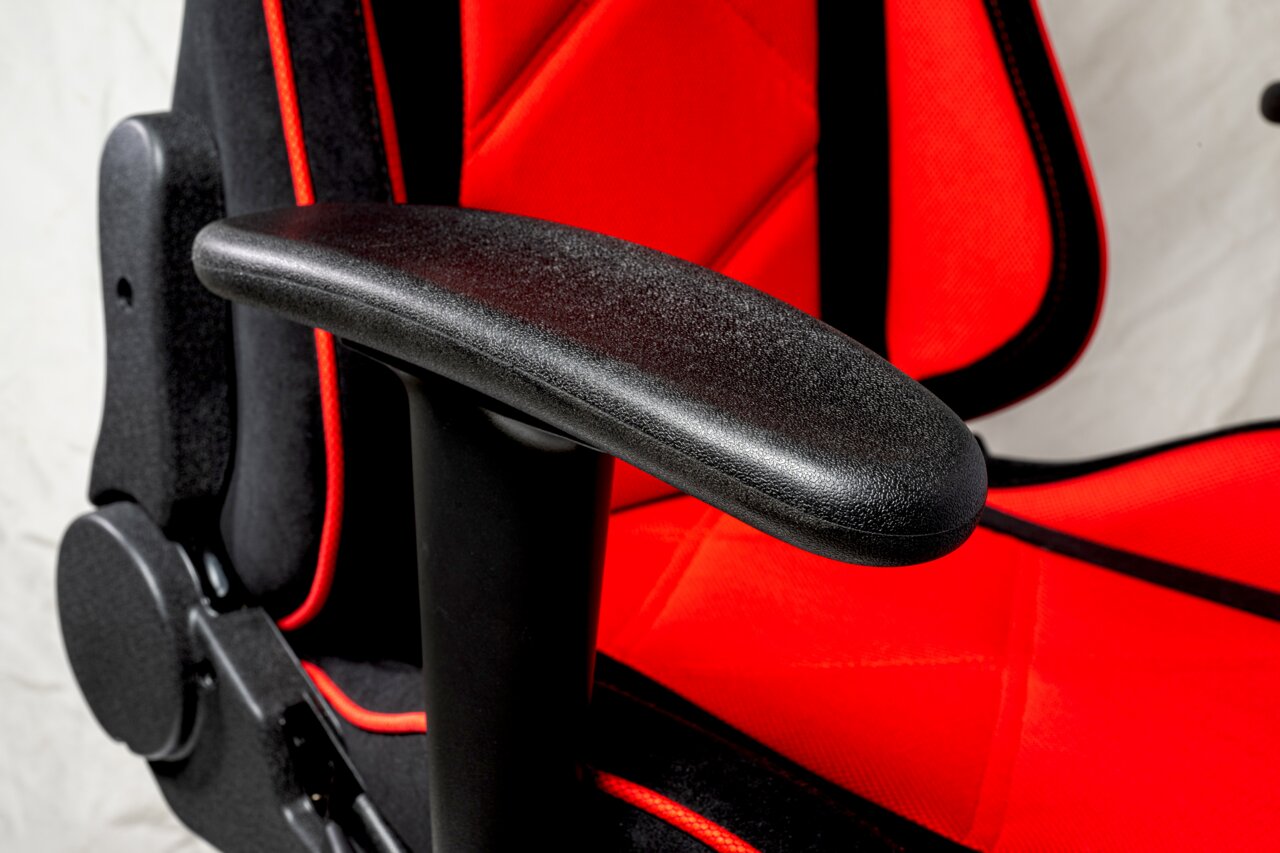 Close-up van een gamingstoel met rode bekleding en zwarte armleuningen, gezien vanaf de zijkant.