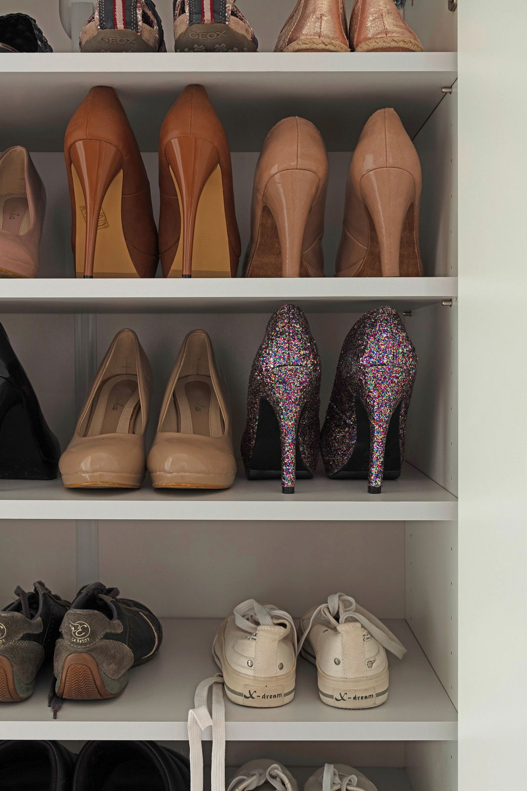 Schuhschrank mit verschiedenen Schuhen, darunter High Heels und Sneakers, aus der frontalen Perspektive.
