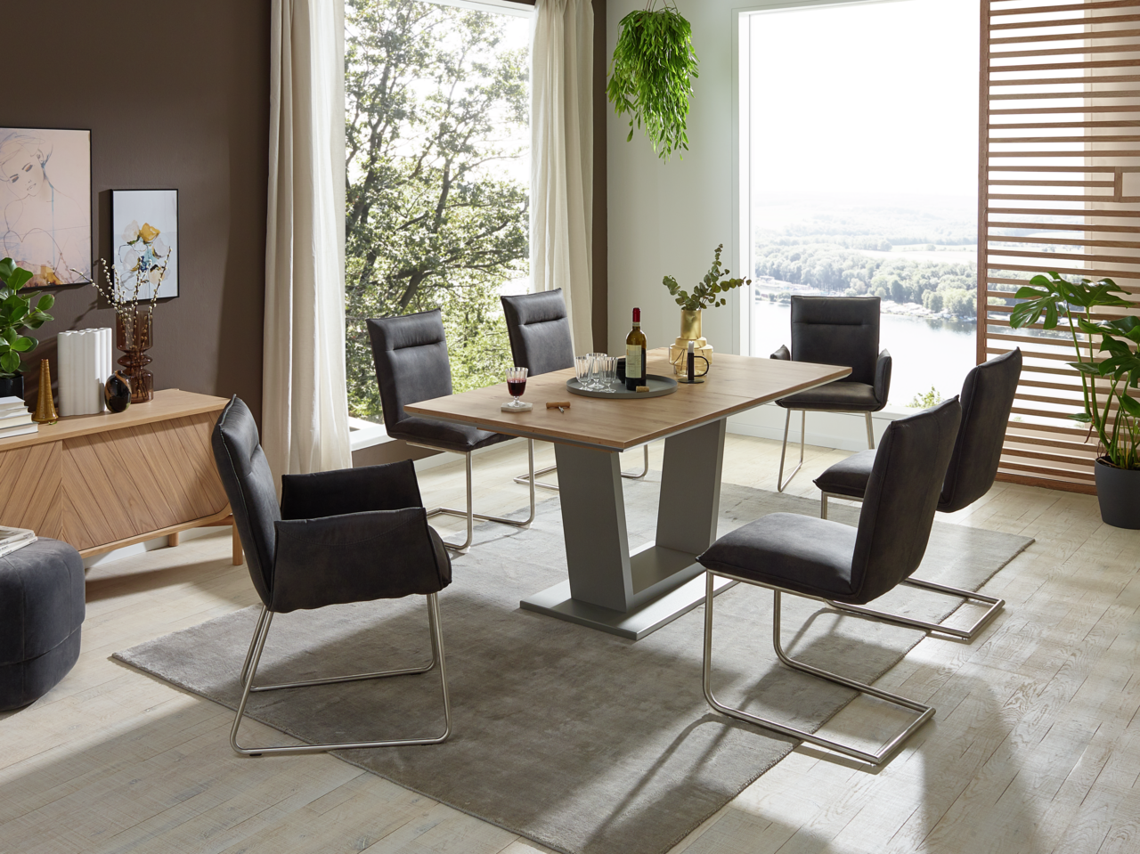 Moderner Essbereich mit einem rechteckigen Holztisch und sechs Freischwinger-Stühlen in einem hellen Raum mit großen Fenstern und Pflanzen. Perspektive: seitliche Ansicht.