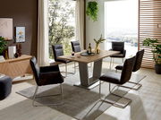 Moderner Essbereich mit einem rechteckigen Holztisch und sechs Freischwinger-Stühlen in einem hellen Raum mit großen Fenstern und Pflanzen. Perspektive: seitliche Ansicht.