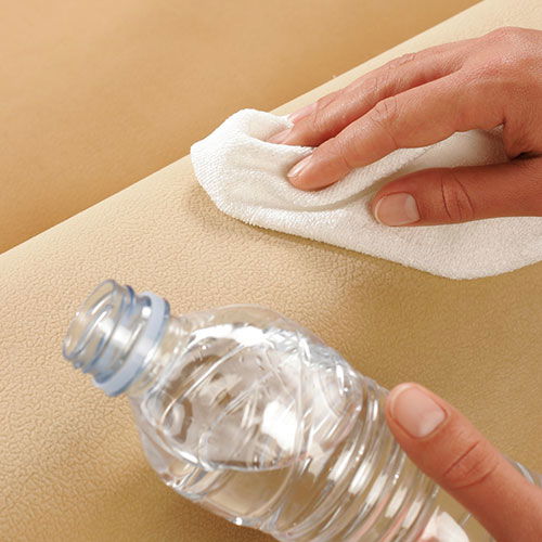 Eine Hand wischt mit einem Tuch über eine beigefarbene Fläche neben einer Wasserflasche.