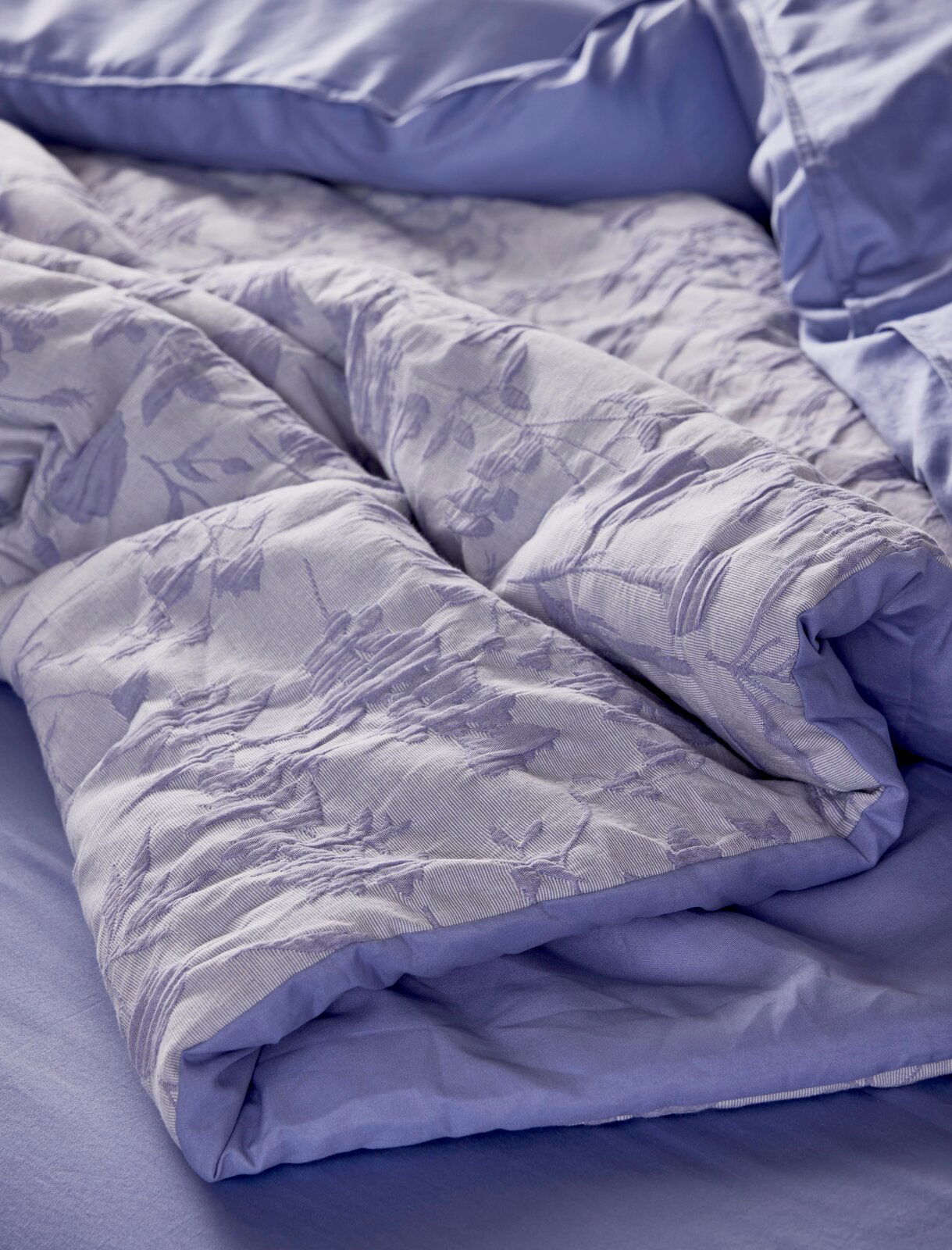 Nahaufnahme einer lila Bettwäsche mit floralem Muster, auf einem Bett drapiert.